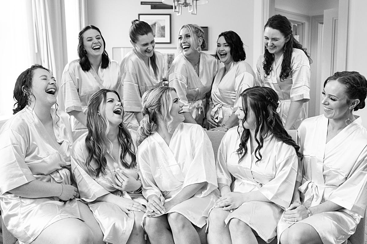 The bridesmaids and the bride in their robes laughing on the couch before they get dressed for photos.